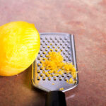 Mesa con un limón y un rallador donde hay ralladura de la piel de lmón.